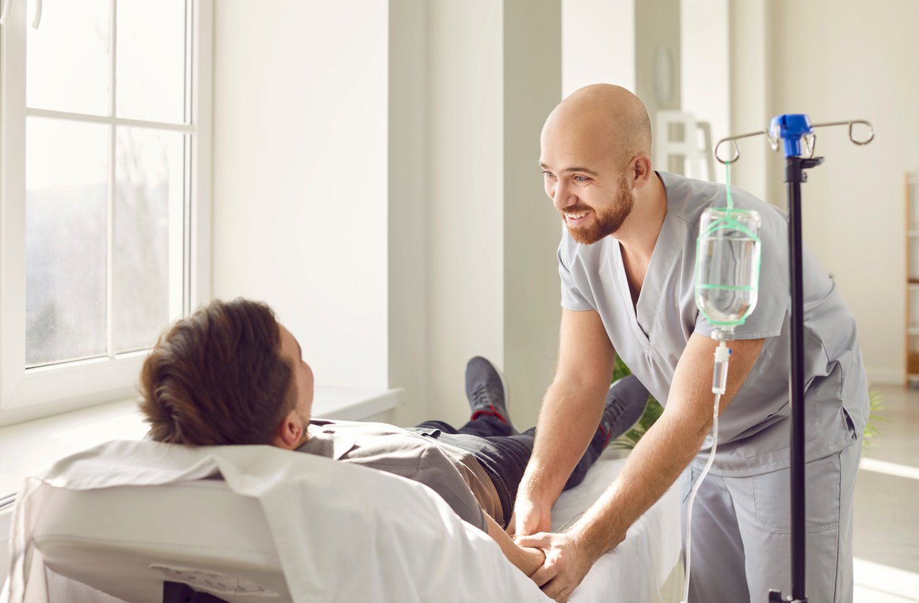 Smiling Medical Nurse Gives Intravenous IV Line Vitamin Infusion to Patient in Hospital